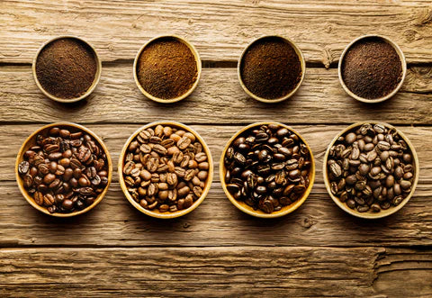 Different stages of roasted coffee beans and ground coffee displayed in wooden bowls on rustic wooden background