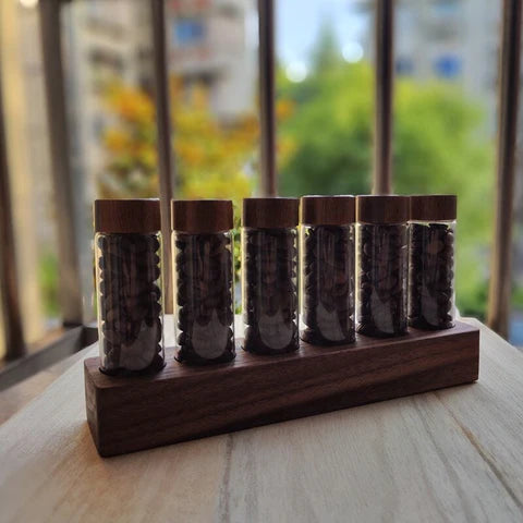 Set of six glass spice jars with wooden lids on a wooden stand, blurred greenery in the background
