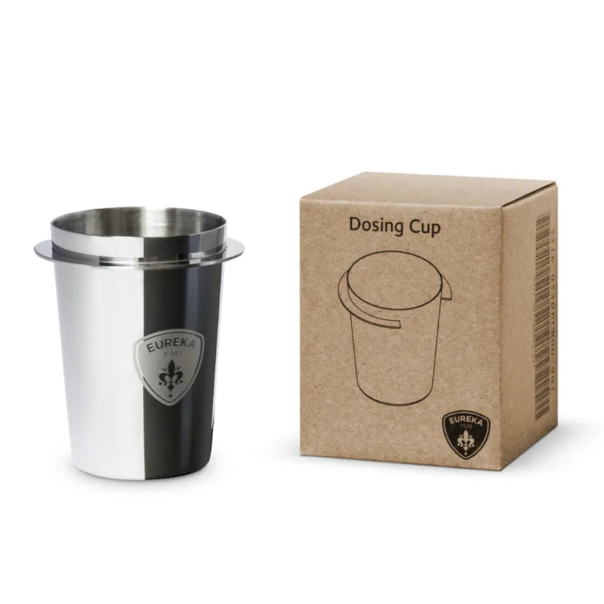 "Eureka espresso dosing cup in brushed stainless steel finish featuring black circular Eureka shield logo, displayed alongside brown kraft paper retail packaging box with 'Dosing Cup' text and line drawing of cup, Eureka logo at bottom"