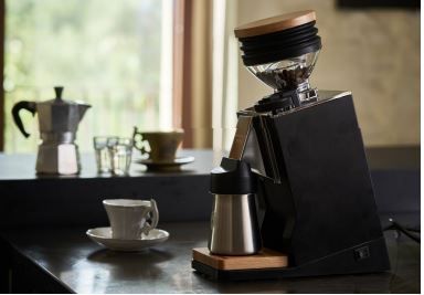 Eureka Mignon Single Dose PRO black grinder on countertop next to coffee mugs and window.