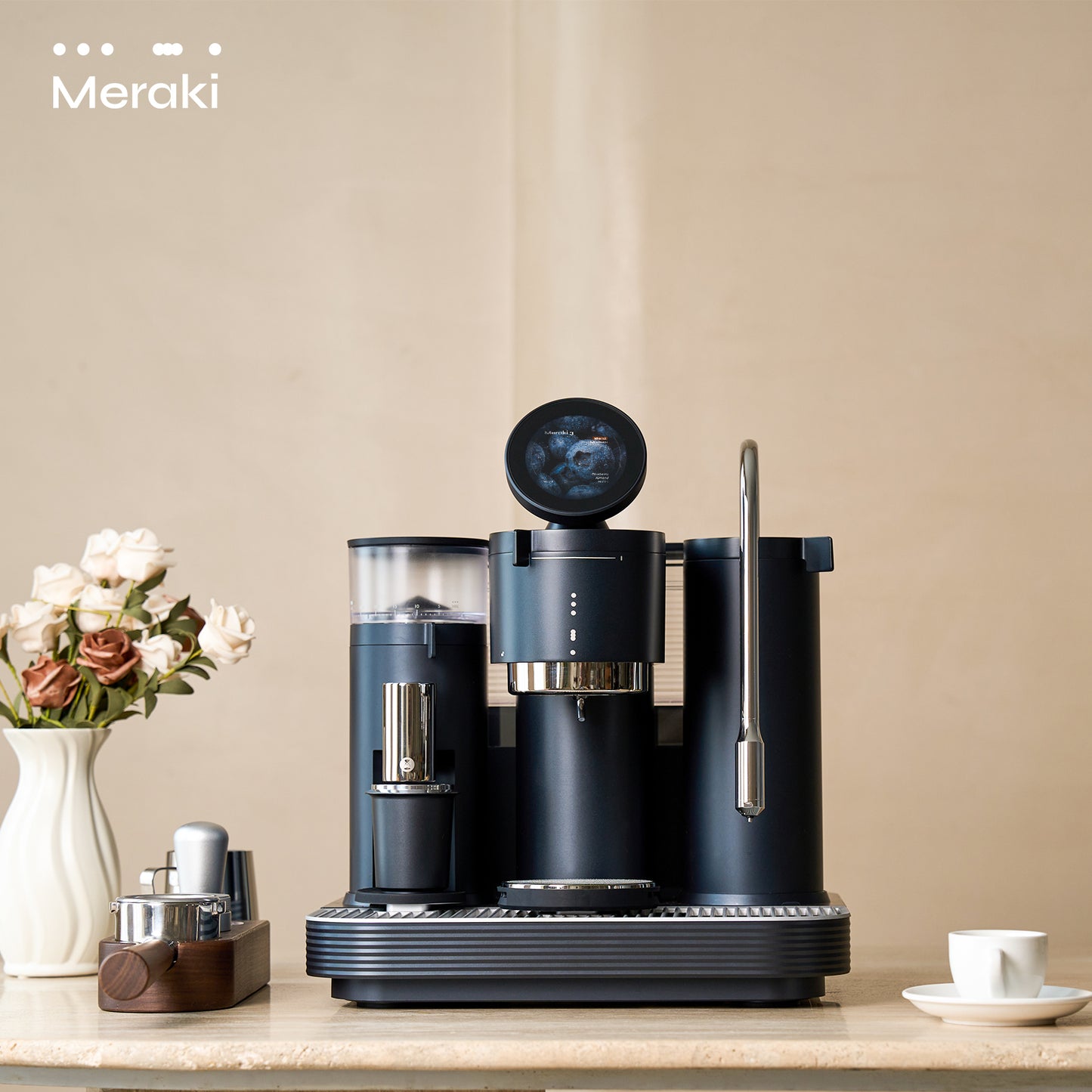 Meraki Espresso Machine black edition on countertop, flowers and mugs in background