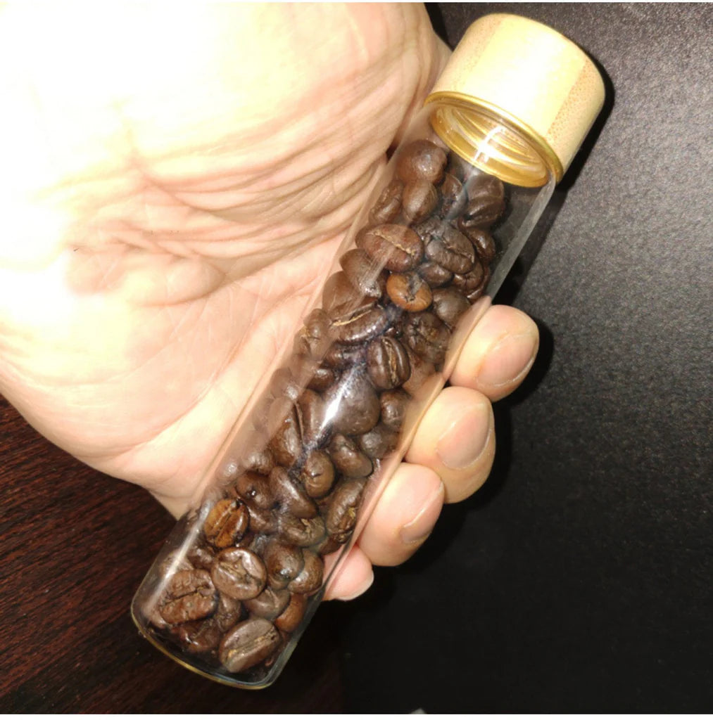 Clear container filled with coffee beans held in a hand against a dark background