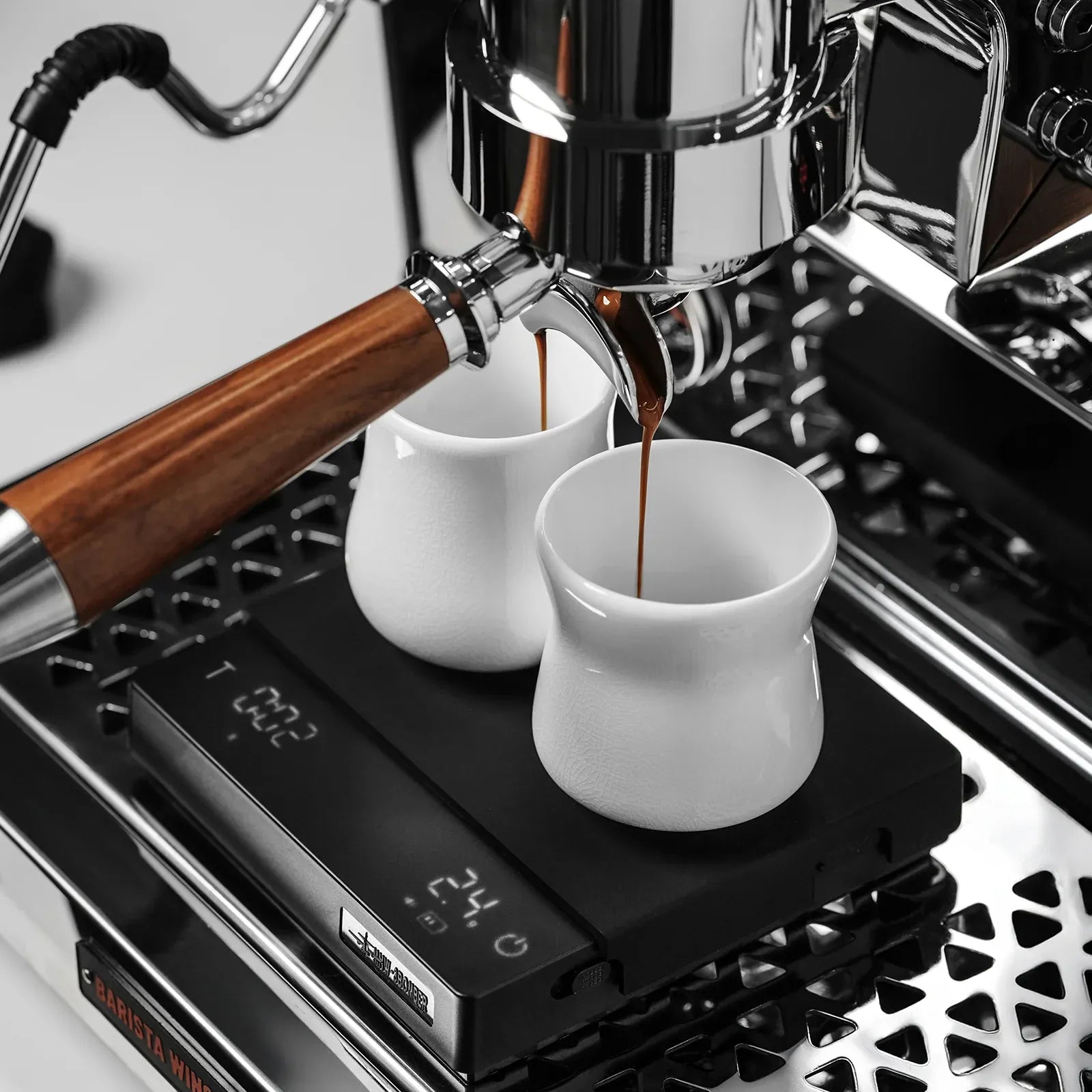 Espresso machine pouring coffee into two white cups on a digital scale.