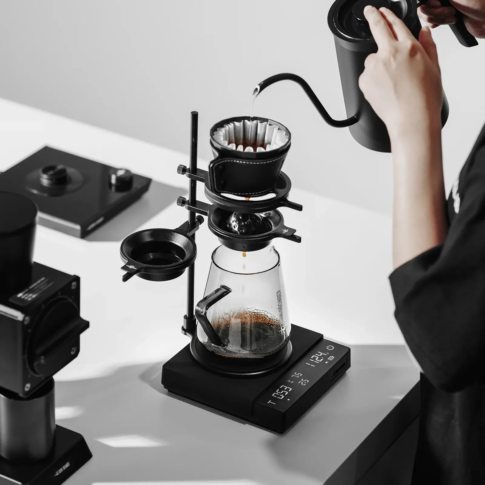 Person making coffee using a manual coffee brewing setup on a white surface.