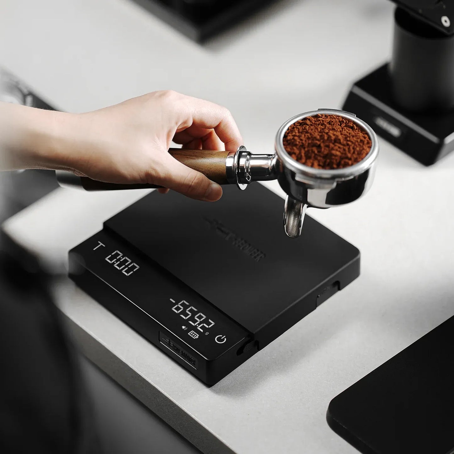 Hand pouring coffee grounds into a portafilter on a digital scale.