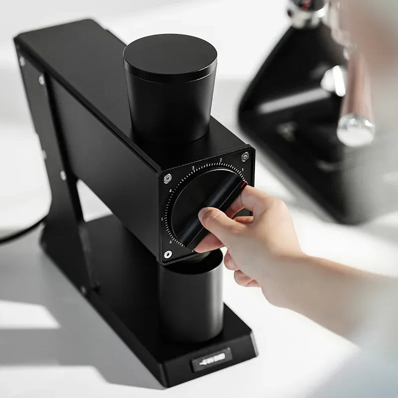 Black coffee grinder with a hand adjusting the settings on a light background