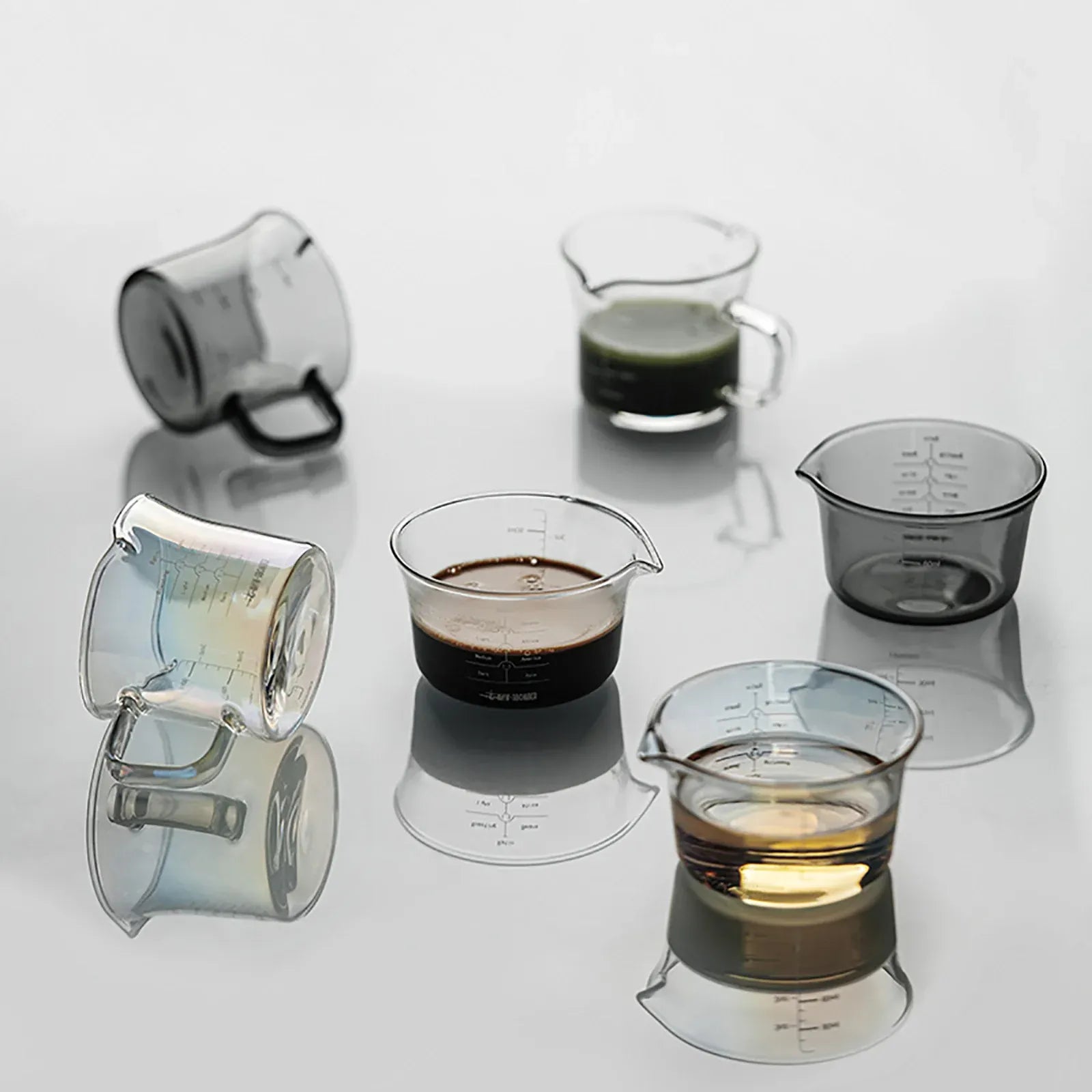 Set of glass measuring cups with different contents on a reflective surface