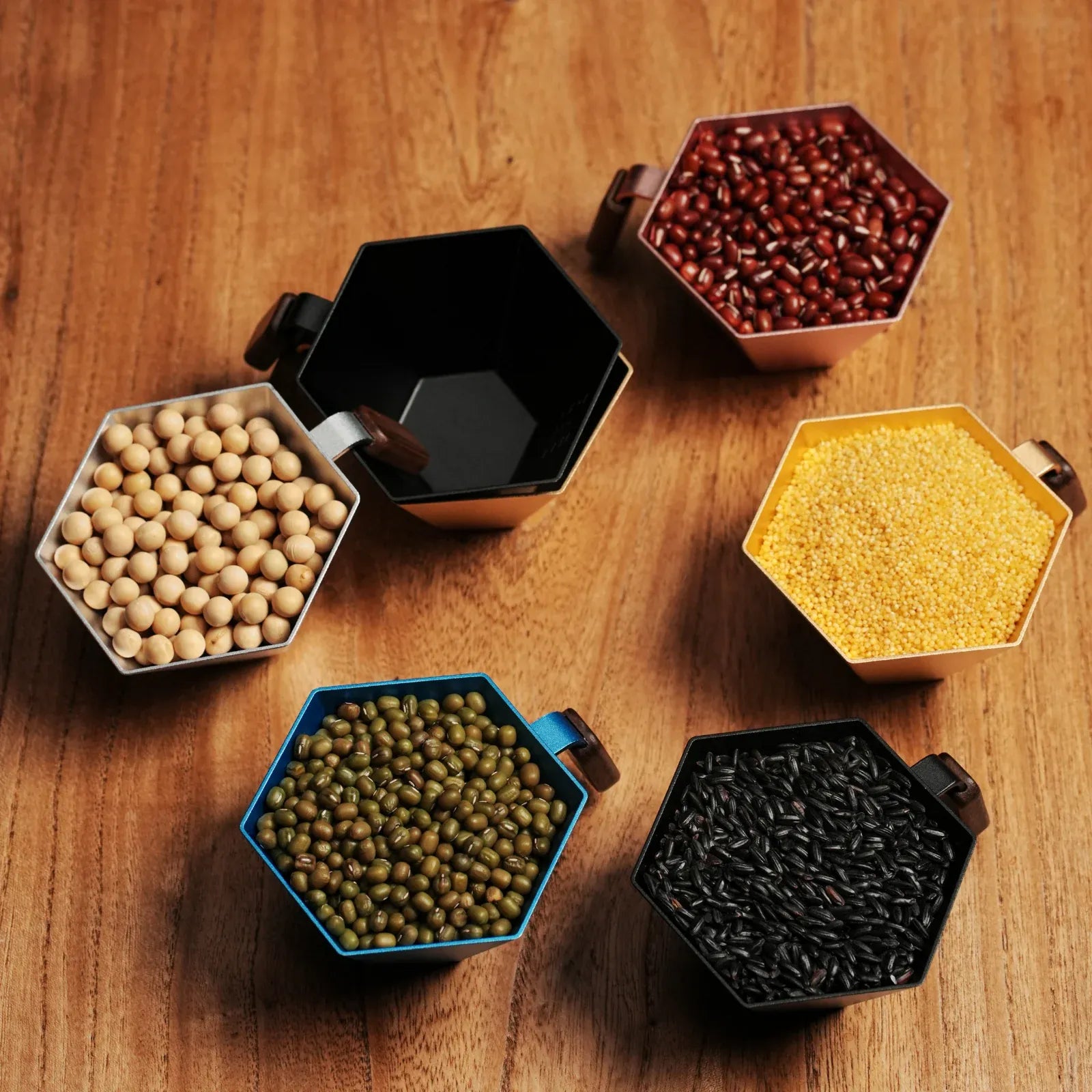 Hexagonal containers with various seeds and a black container on a wooden surface