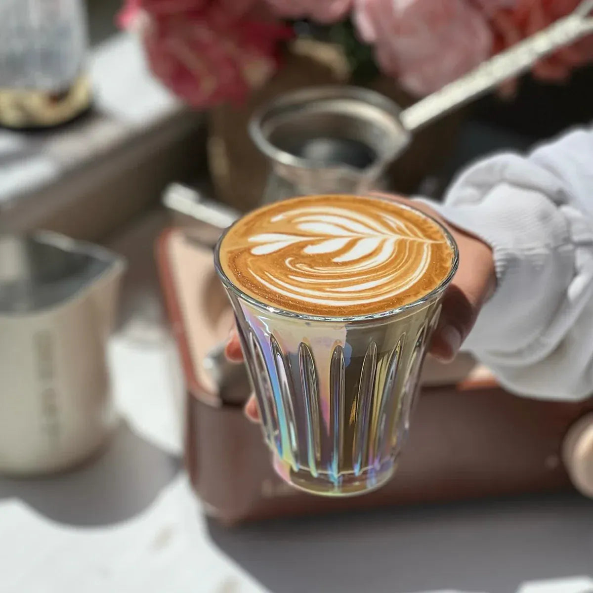 Glass of coffee with latte art held by a person, with a blurred background