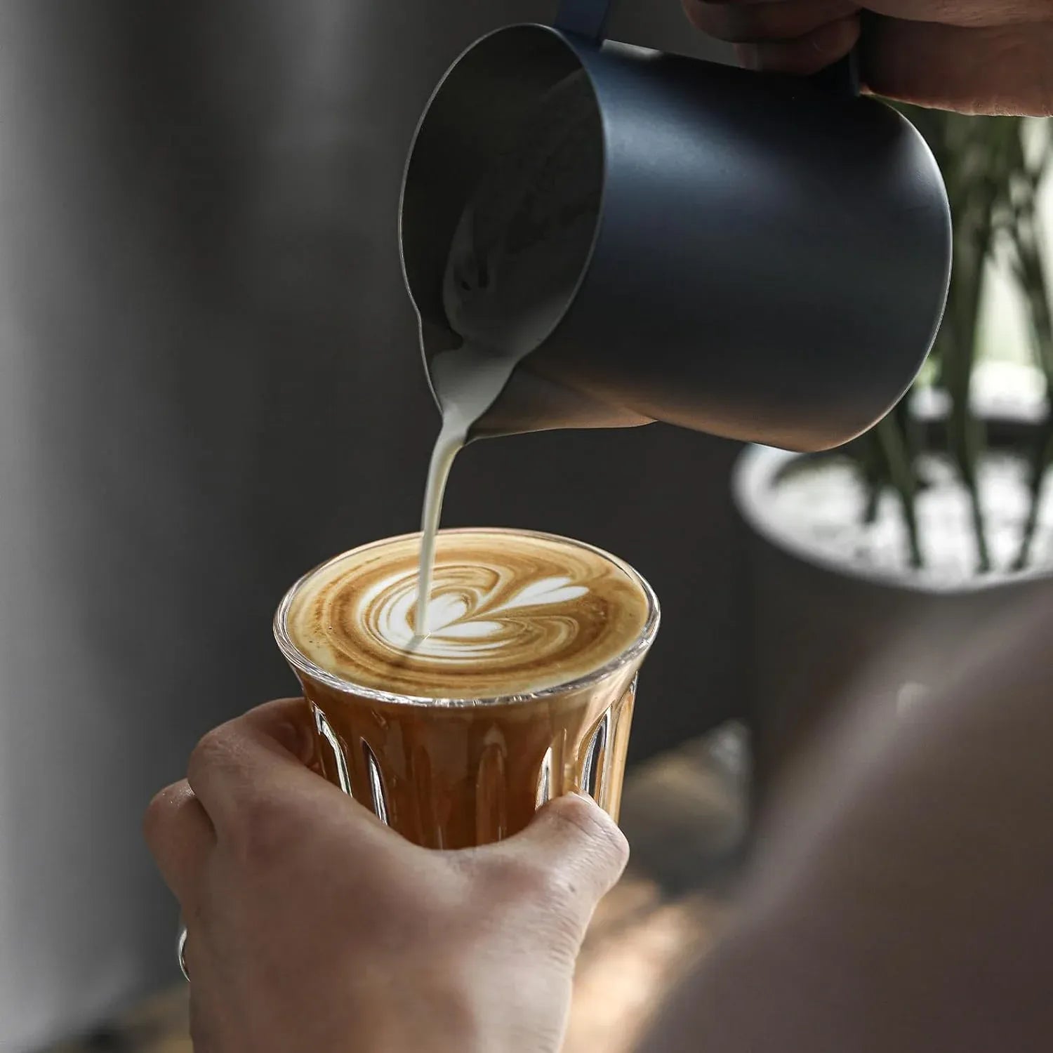 Person pouring steamed milk into a cup of coffee to create latte art.