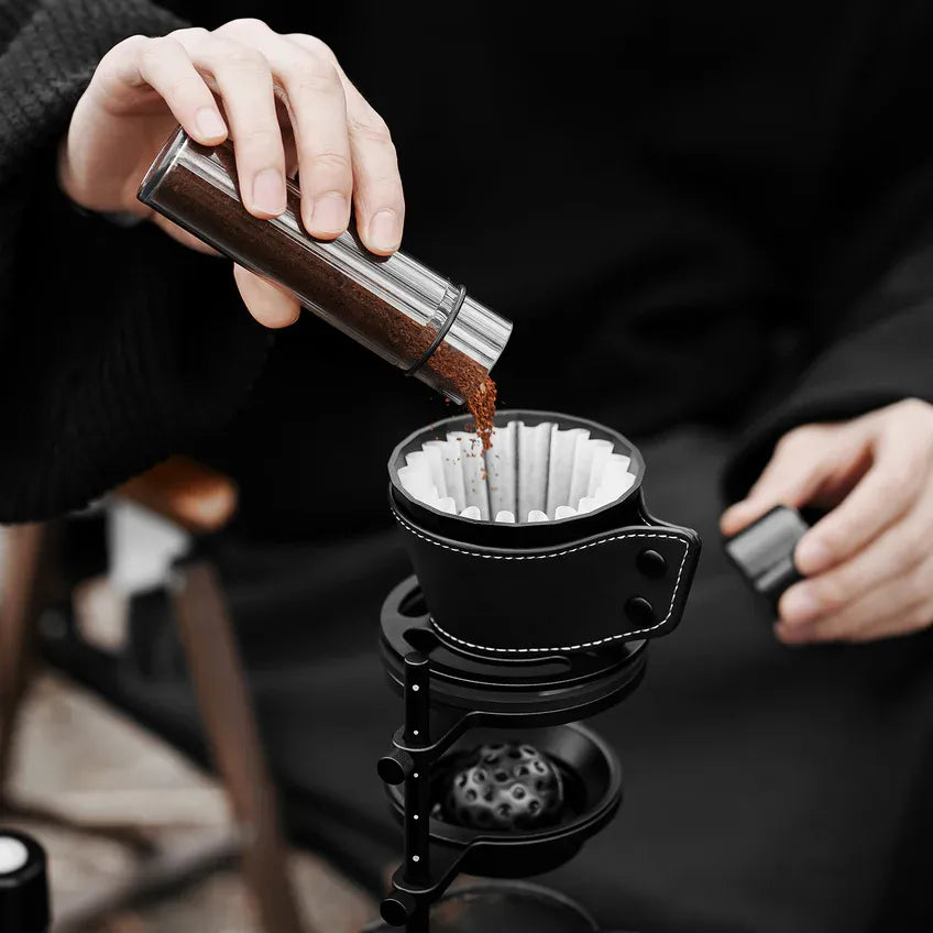 Person pouring coffee grounds into a coffee filter with a black coffee press in the background.