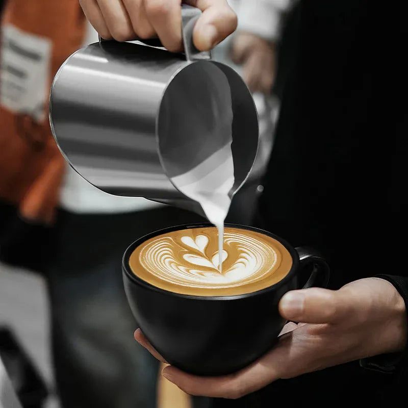 Person pouring milk into a cup of coffee to create latte art.