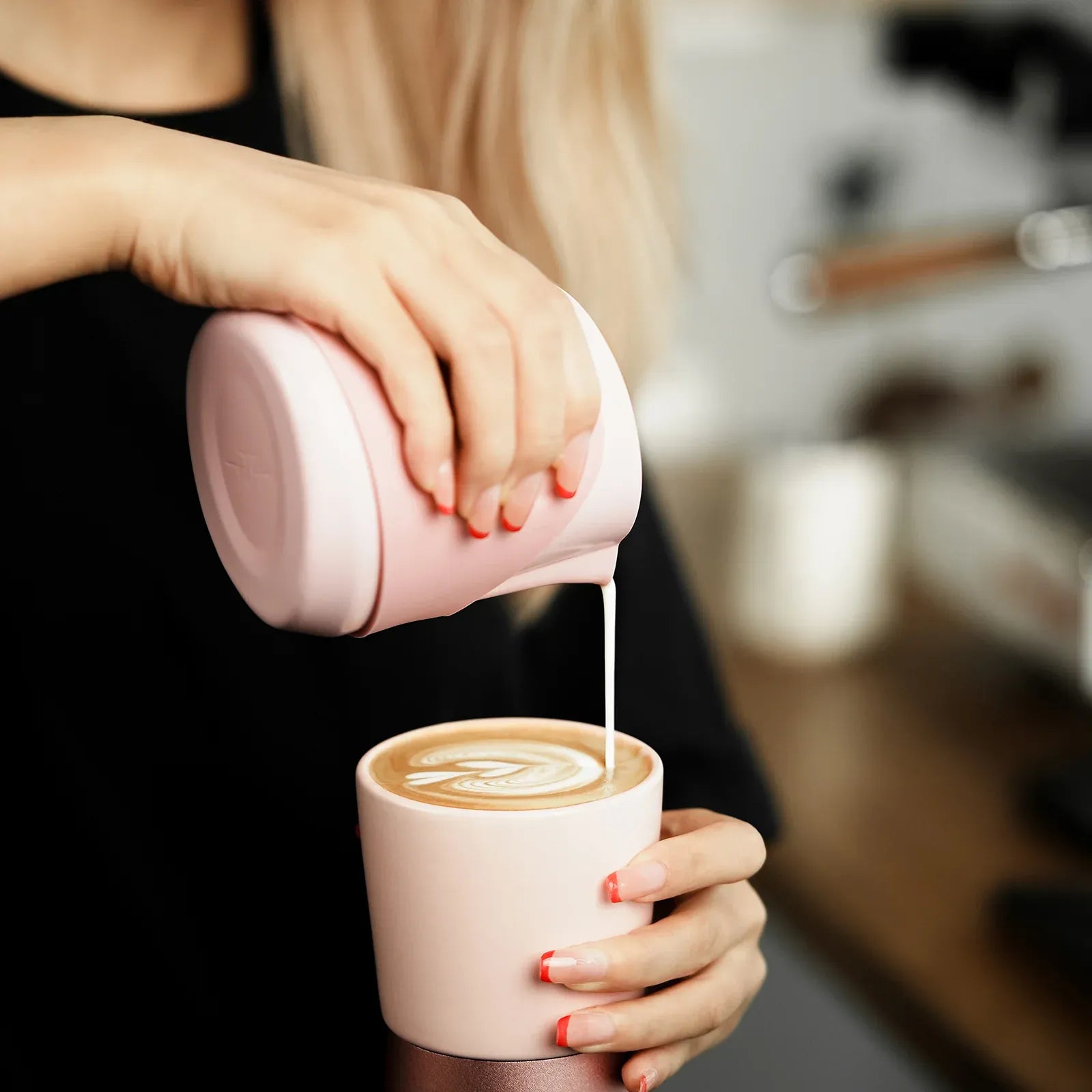 Person pouring milk from a pink pitcher into a pink mug with a blurred background