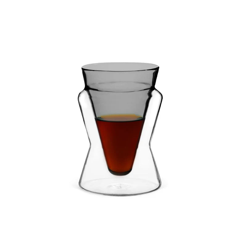 Clear glass tumbler with a small amount of red liquid on a white background