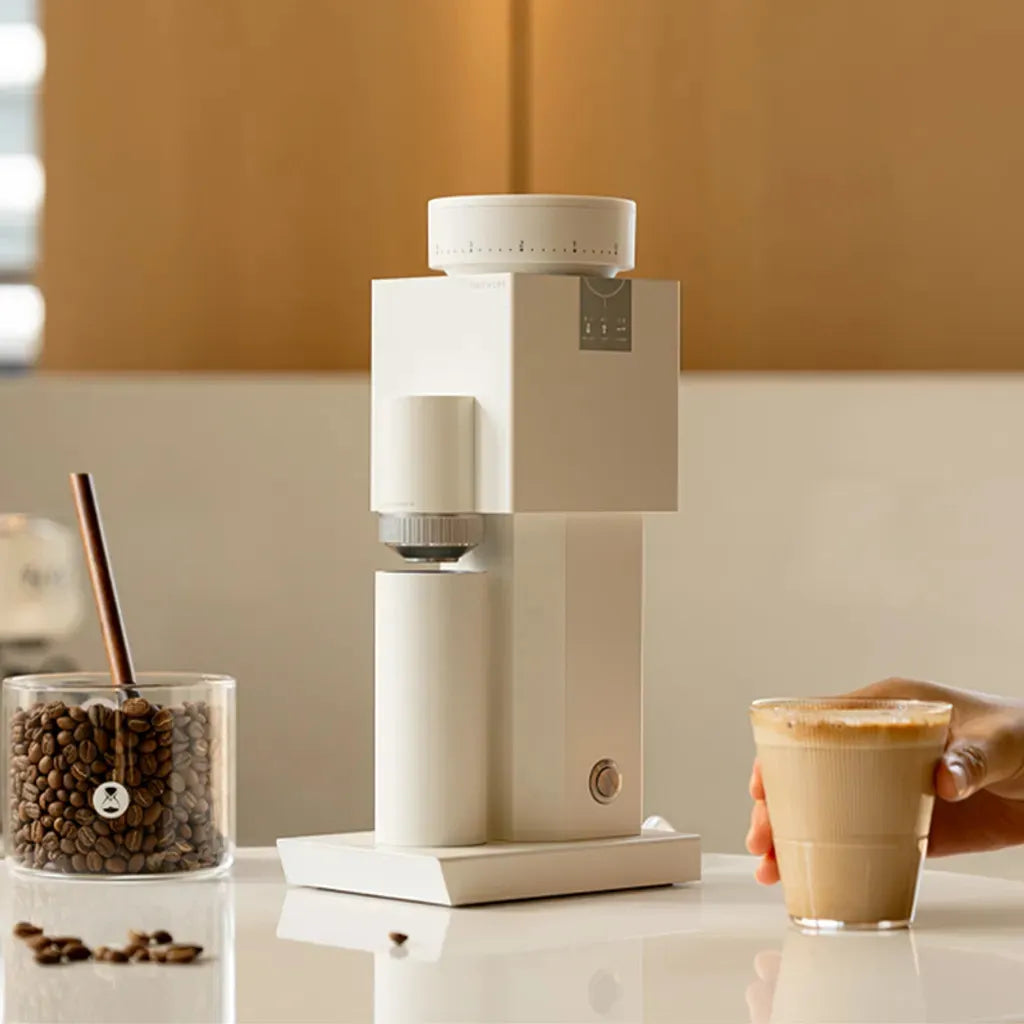 White coffee grinder on a kitchen counter with a glass of coffee and coffee beans.