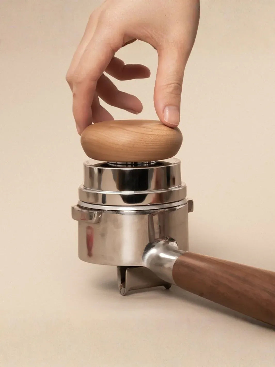 Hand using a manual coffee grinder with wooden handle and top on a beige background