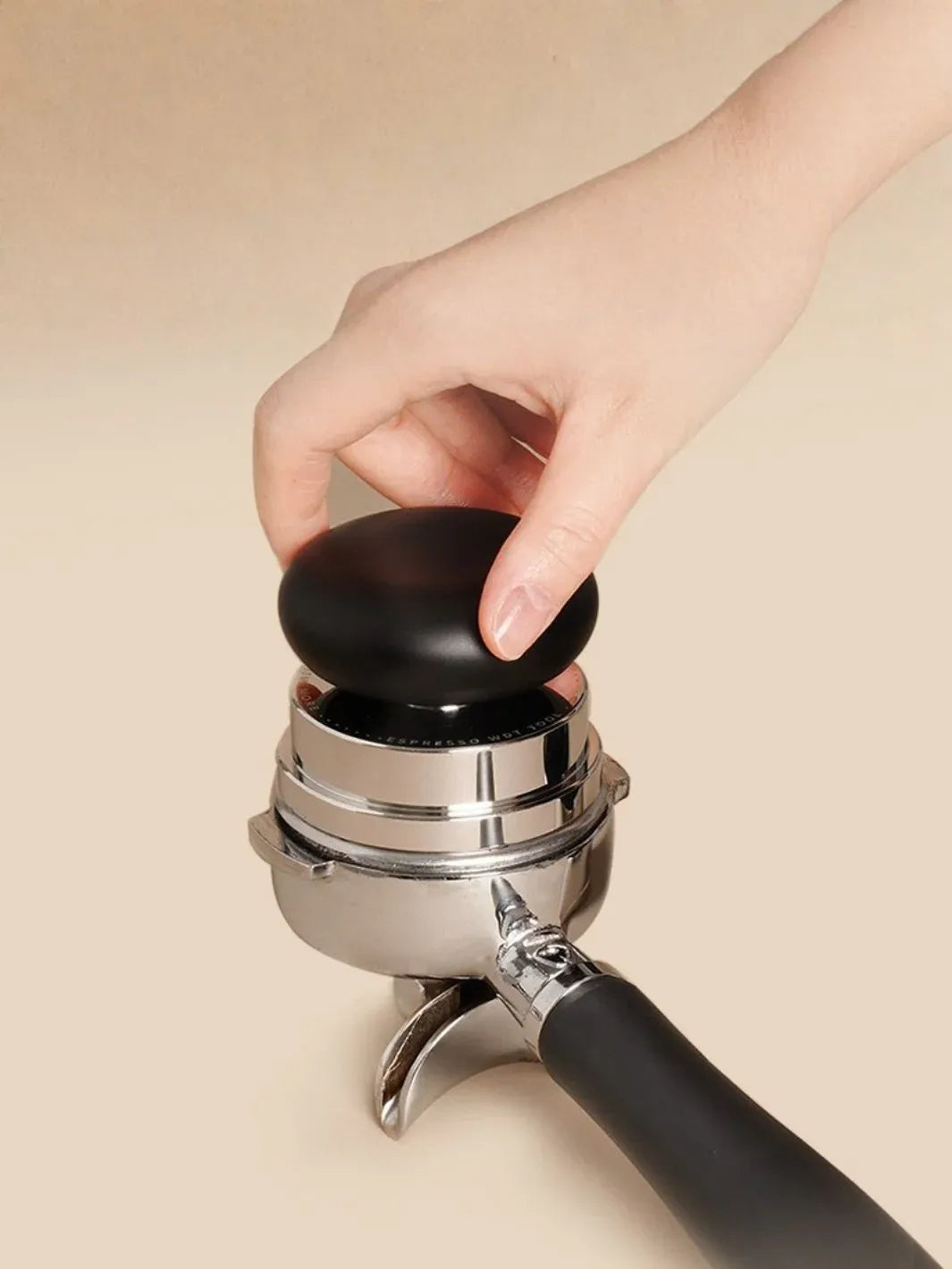 Hand using a coffee tamp on a beige background