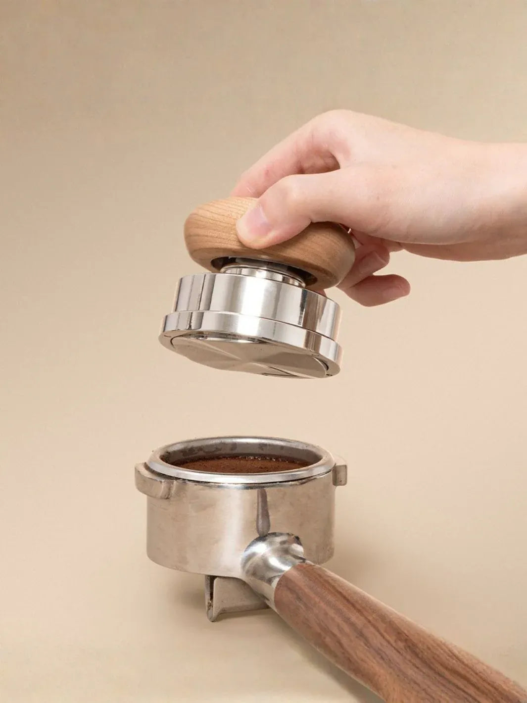 Hand using a coffee tamper to compress coffee grounds into a portafilter on a beige background