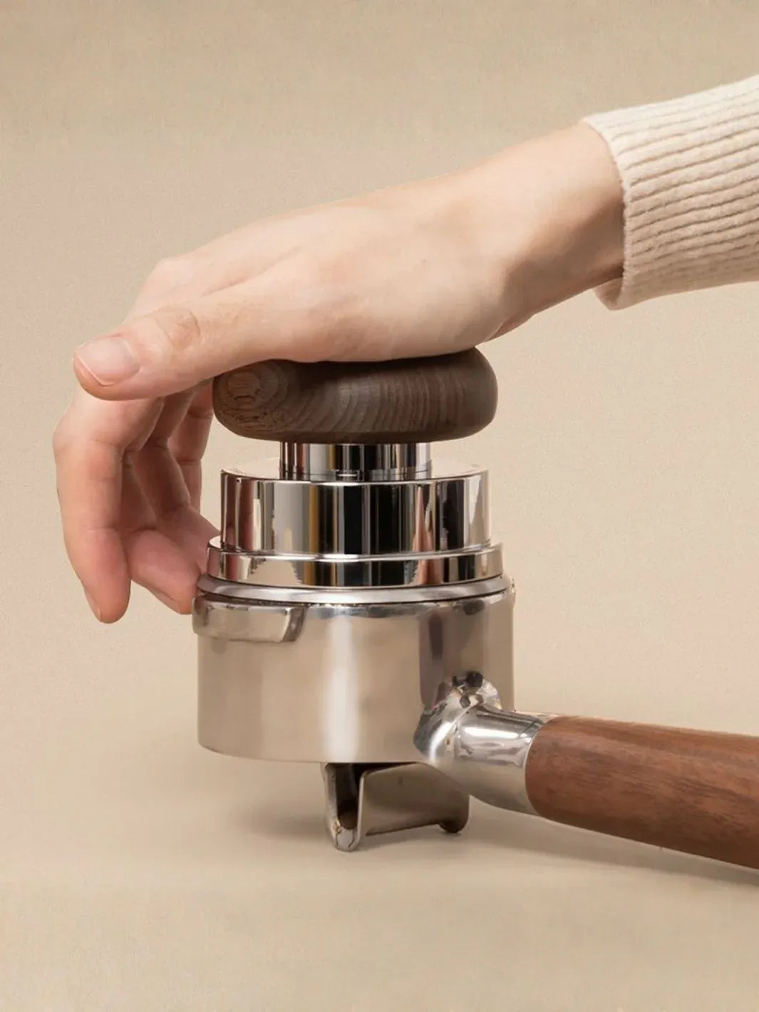 Hand holding a metal coffee press with wooden handles on a beige background