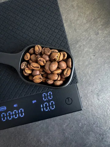 Black scoop filled with coffee beans on a digital scale with a dark background