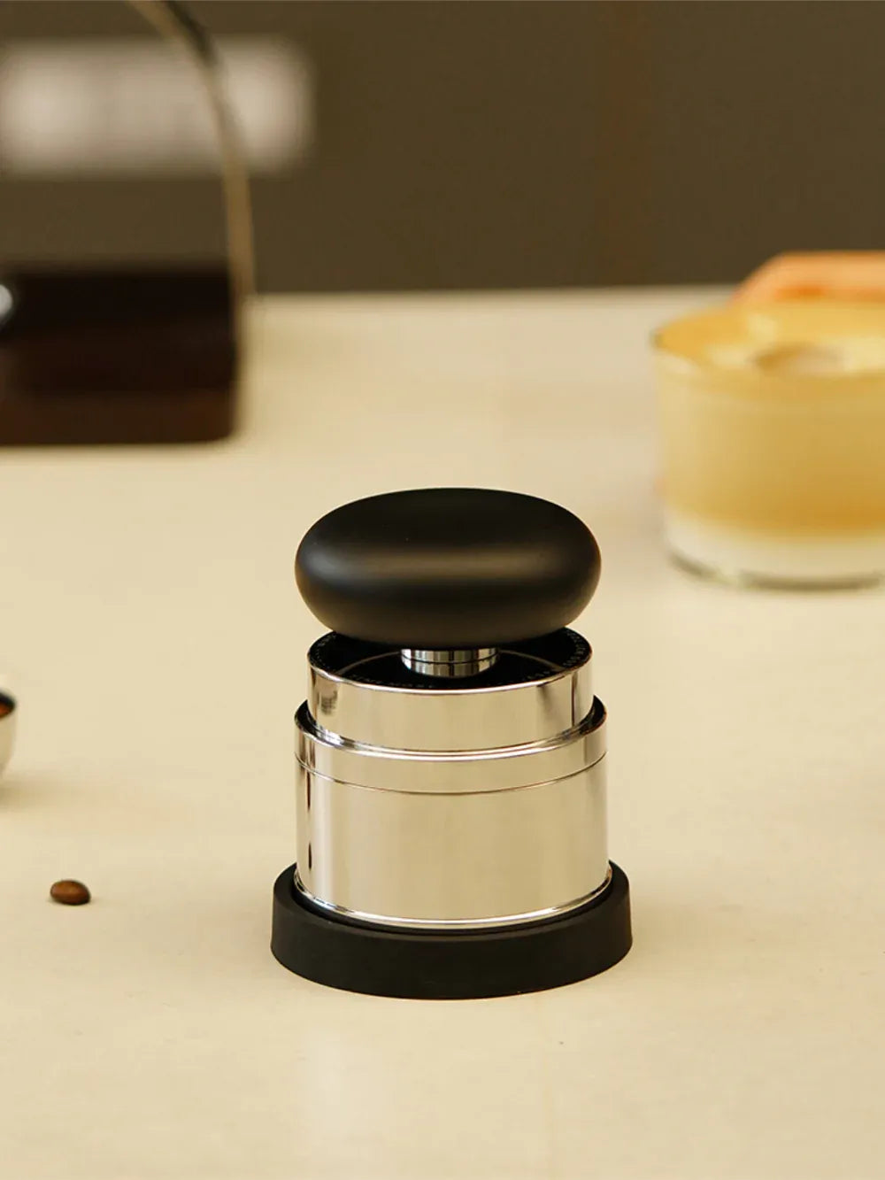 Coffee tamp on a light surface with blurred coffee beans and container in the background
