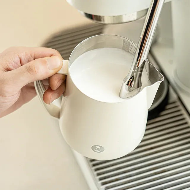 Person using a milk frothing pitcher with a coffee machine.