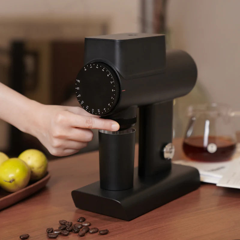 Black coffee grinder on a wooden table with coffee beans and a blurred background