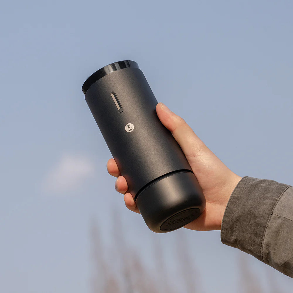 Hand holding a black travel mug against a blurred natural background
