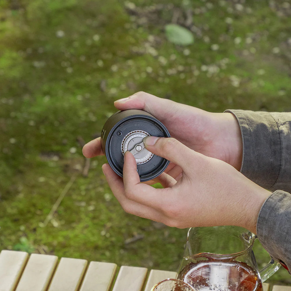 Person holding a coffee maker with a blurred green outdoor background