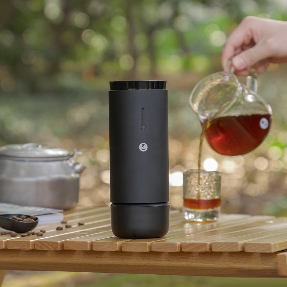 Black portable coffee maker on a wooden table with a blurred natural background