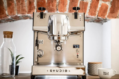 Dalla Corte Studio espresso machine installed in a café setting on wooden counter with rustic brick backdrop