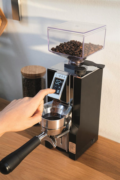 Eureka Mignon Libra dosing funnel coffee grinder with hand pointing at digital display filled with coffee beans on wooden countertop